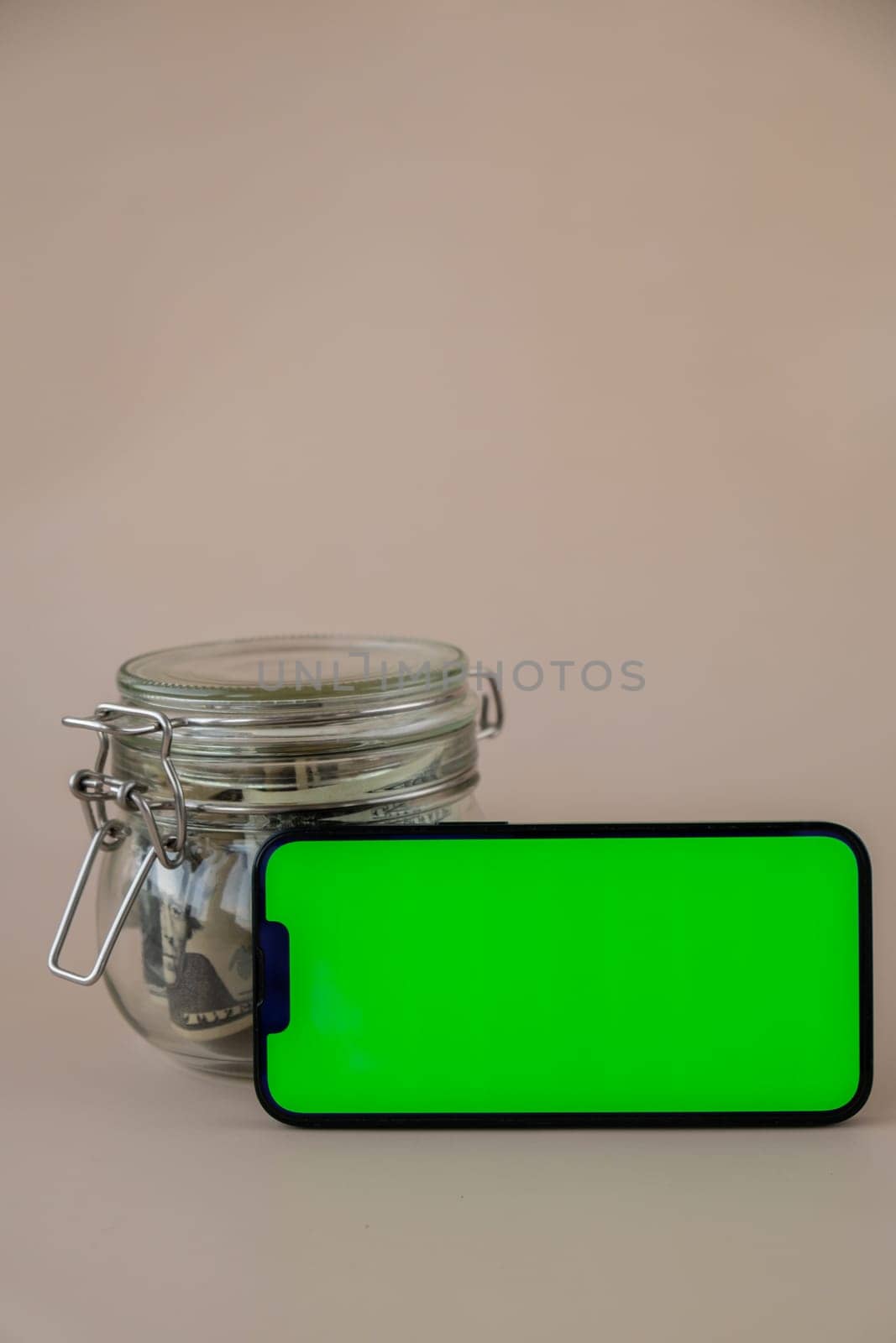 Chrome key smartphone screen mock up template in horizontal position on beige background. Copy space App website advertising. Jar filled with dollars cash. Concept of Mobile application and technology business savings.