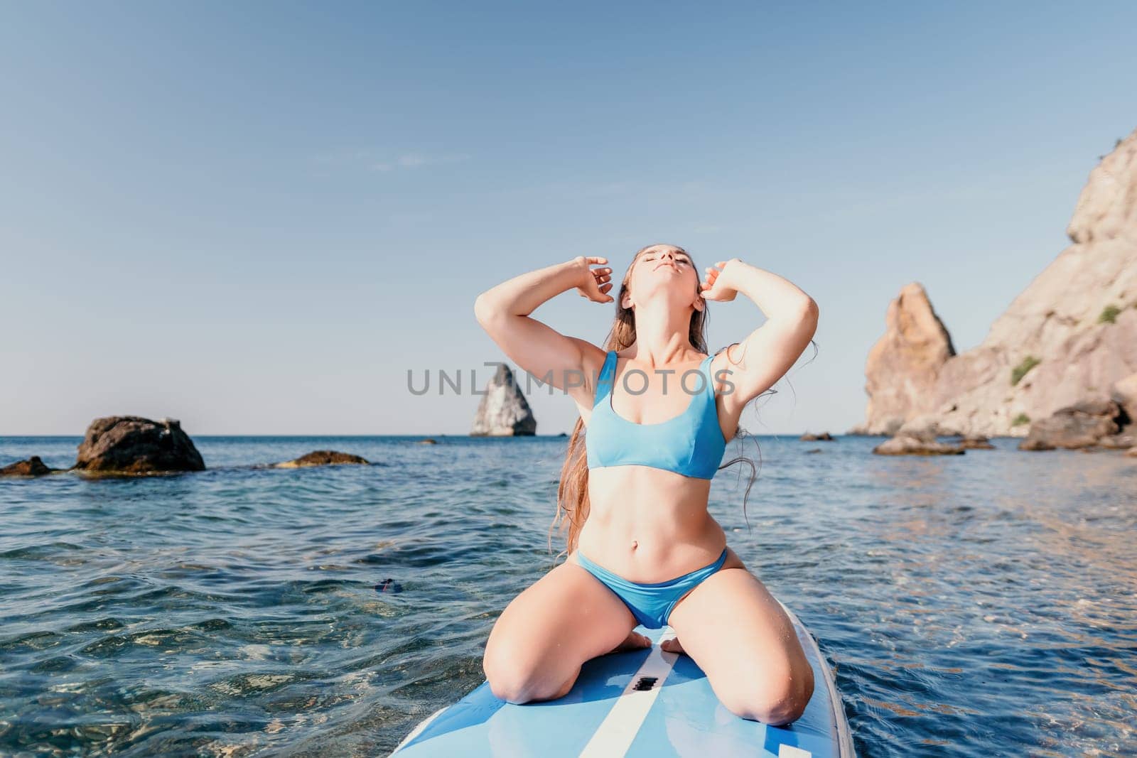 Close up shot of happy young caucasian woman looking at camera and smiling. Cute woman portrait in bikini posing on a volcanic rock high above the sea