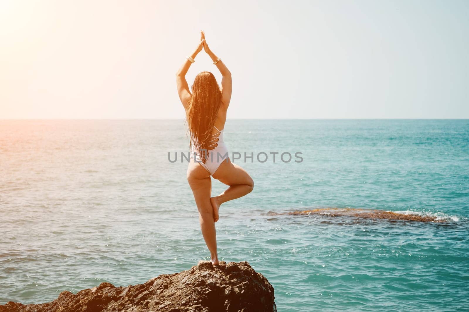 Woman sea yoga. Back view of free calm happy satisfied woman with long hair standing on top rock with yoga position against of sky by the sea. Healthy lifestyle outdoors in nature, fitness concept