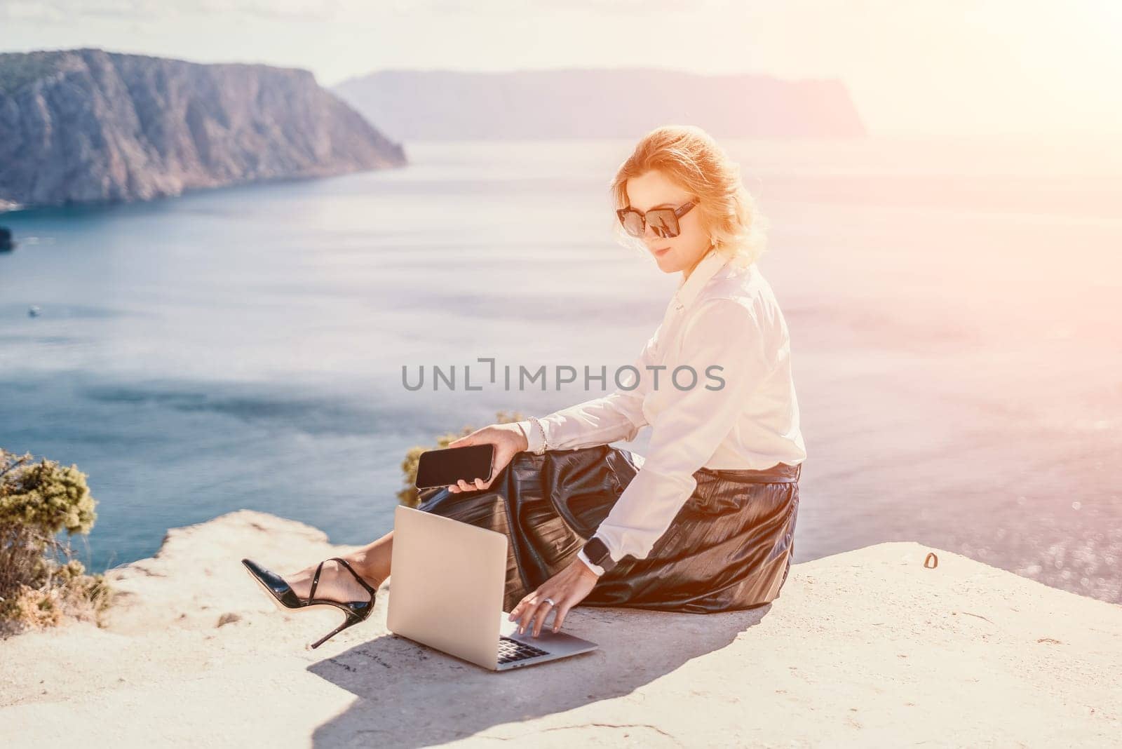 Digital nomad, Business woman working on laptop by the sea. Pretty lady typing on computer by the sea at sunset, makes a business transaction online from a distance. Freelance, remote work on vacation by panophotograph