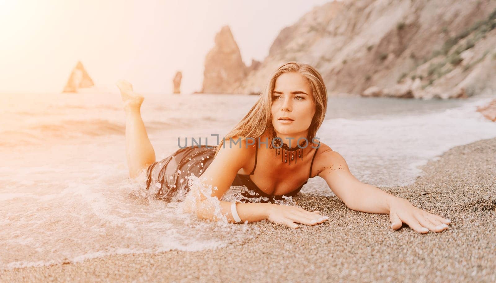 Woman summer travel sea. Happy tourist in black dress enjoy taking picture outdoors for memories. Woman traveler posing on sea beach surrounded by volcanic mountains, sharing travel adventure journey by panophotograph