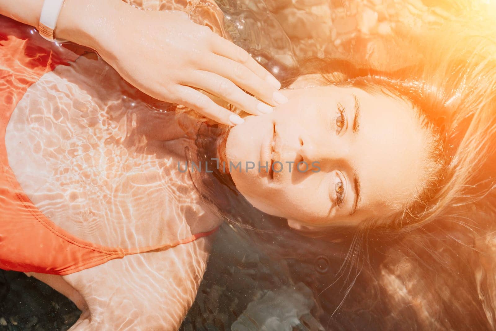 Woman travel portrait. close-up portrait of a happy woman with long hair in a red bikini, floating in water and smiling at the camera. by panophotograph