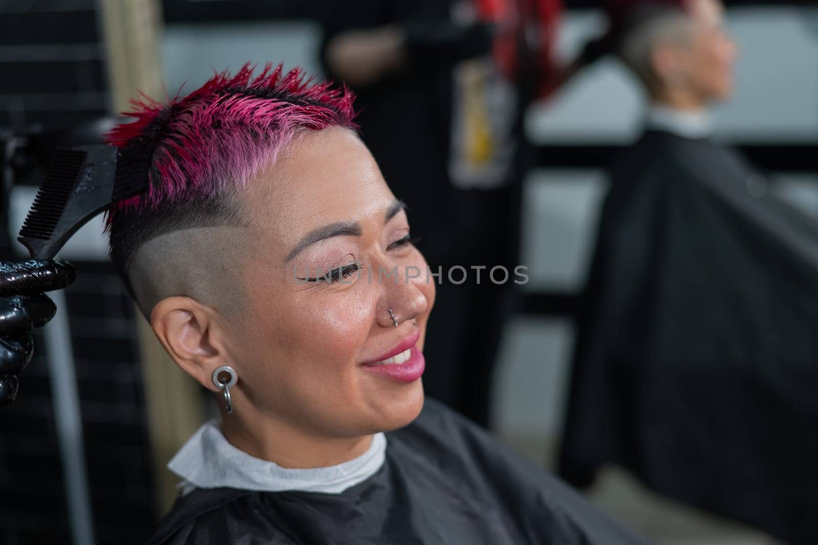 The hairdresser dyes the hair of an Asian woman in pink. Short extreme haircut. by mrwed54