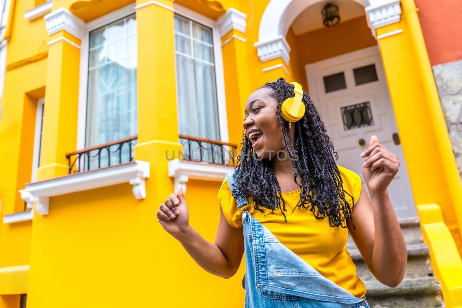 Low angle view photo of a cool african young woman dancing listening to music in the street outside a yellow house