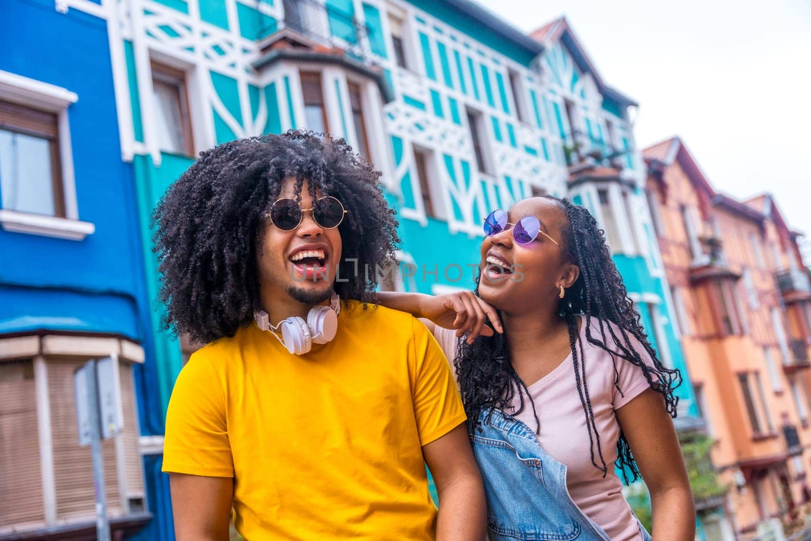 Happy african cool friends with sunglasses and denim casual clothes laughing and chatting in a colorful street