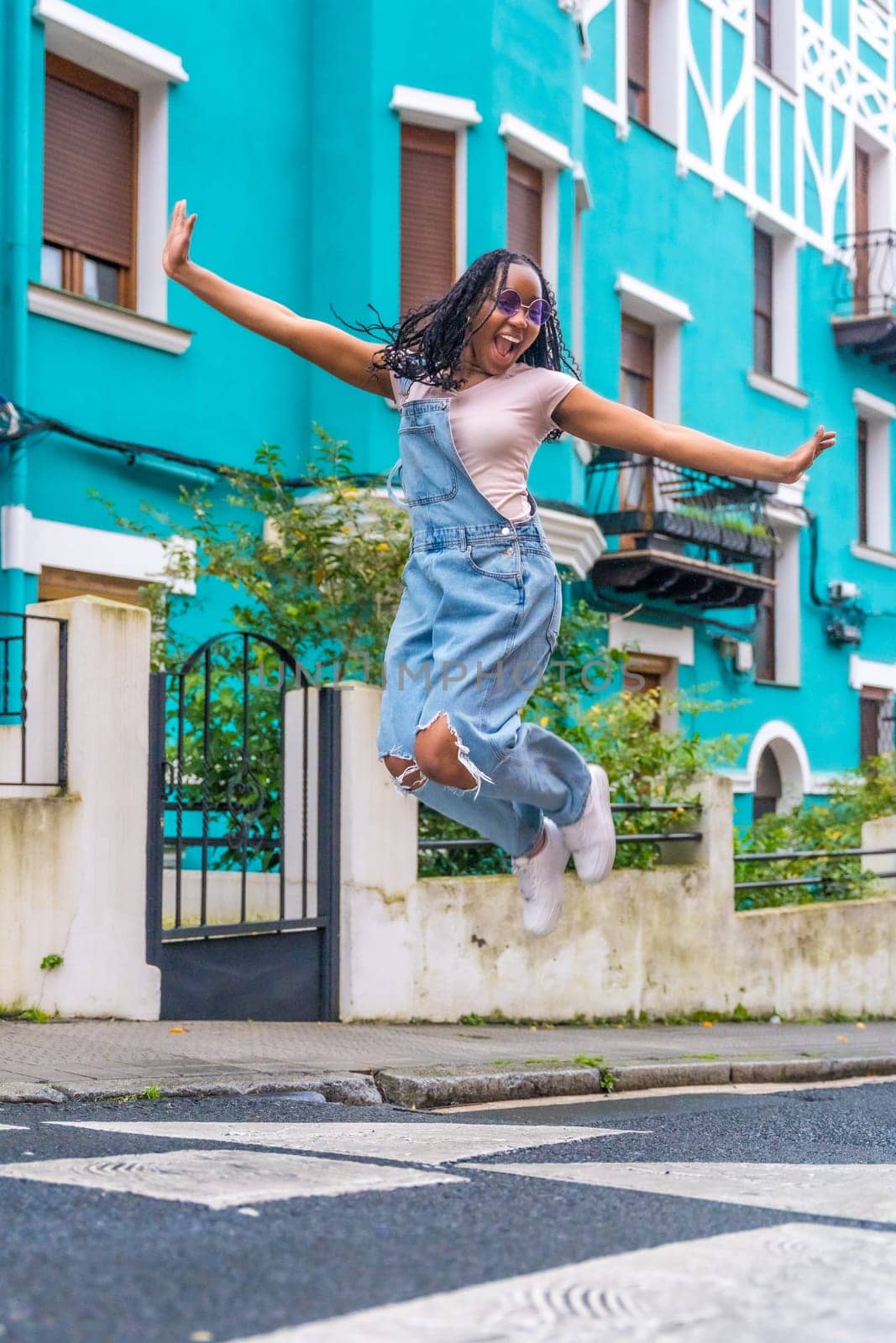 Vertical photo full length of a happy and free african woman jumping in a colorful street