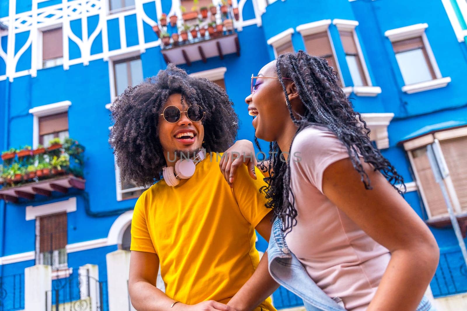Happy afro casual friends strolling in a neighborhood with blue colorful houses