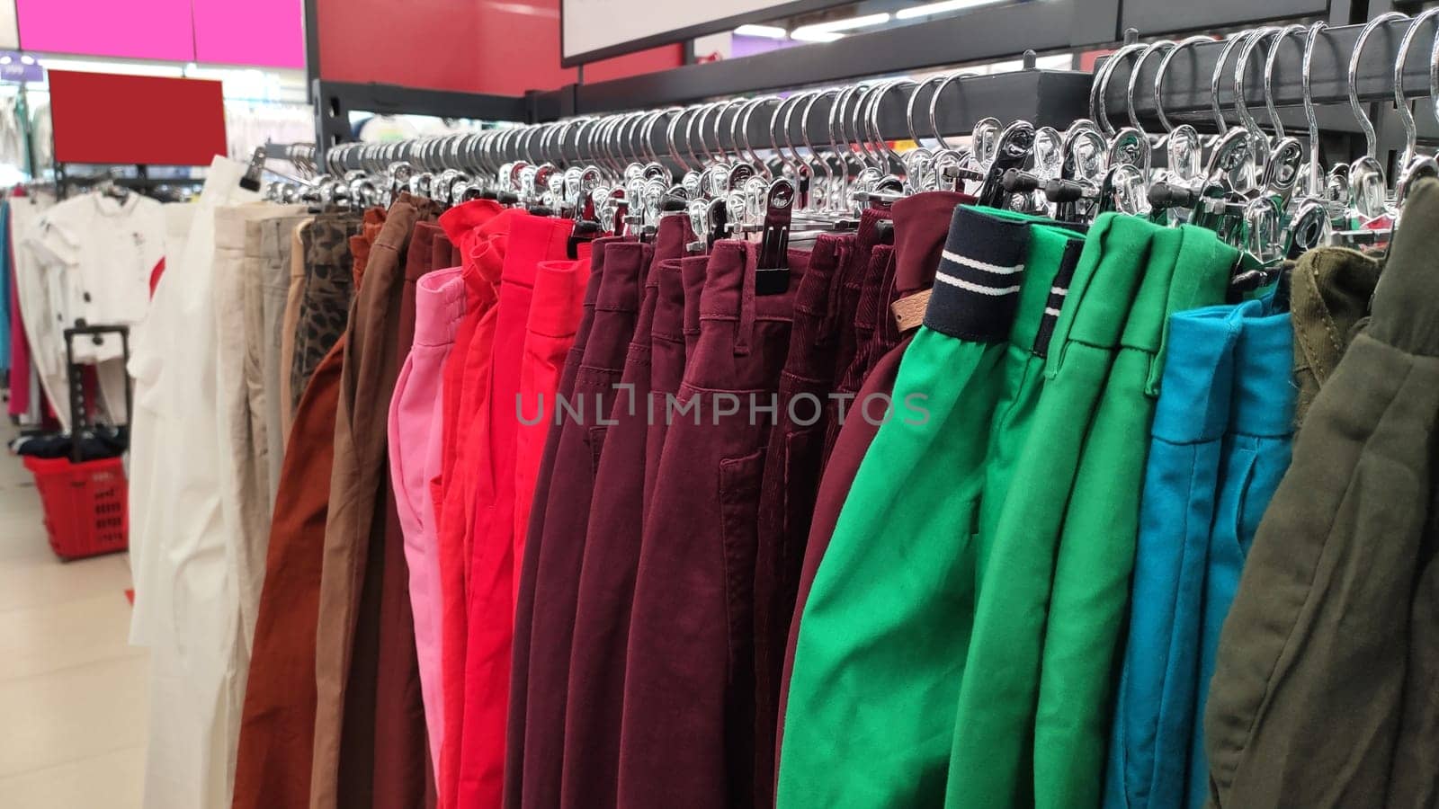 Row of different colorful pants trousers on hanger in shop. Close up