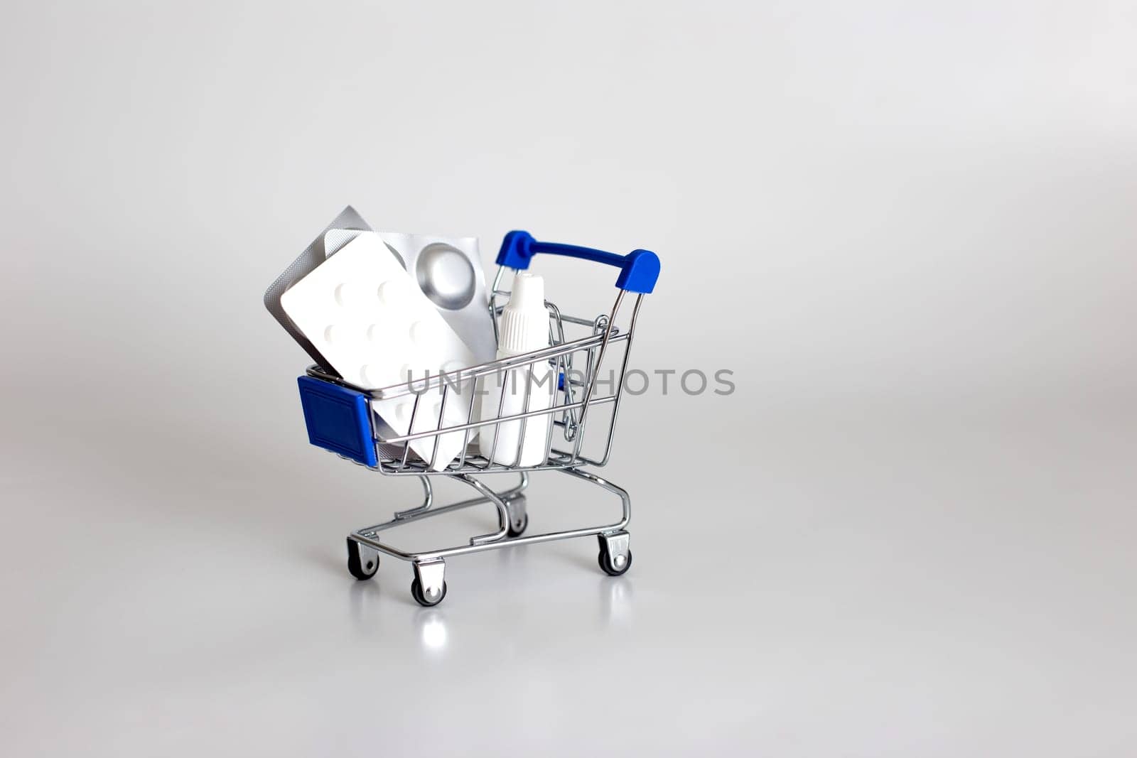White and silver blisters of pills and drops in a small supermarket trolley on a white background. Copy space