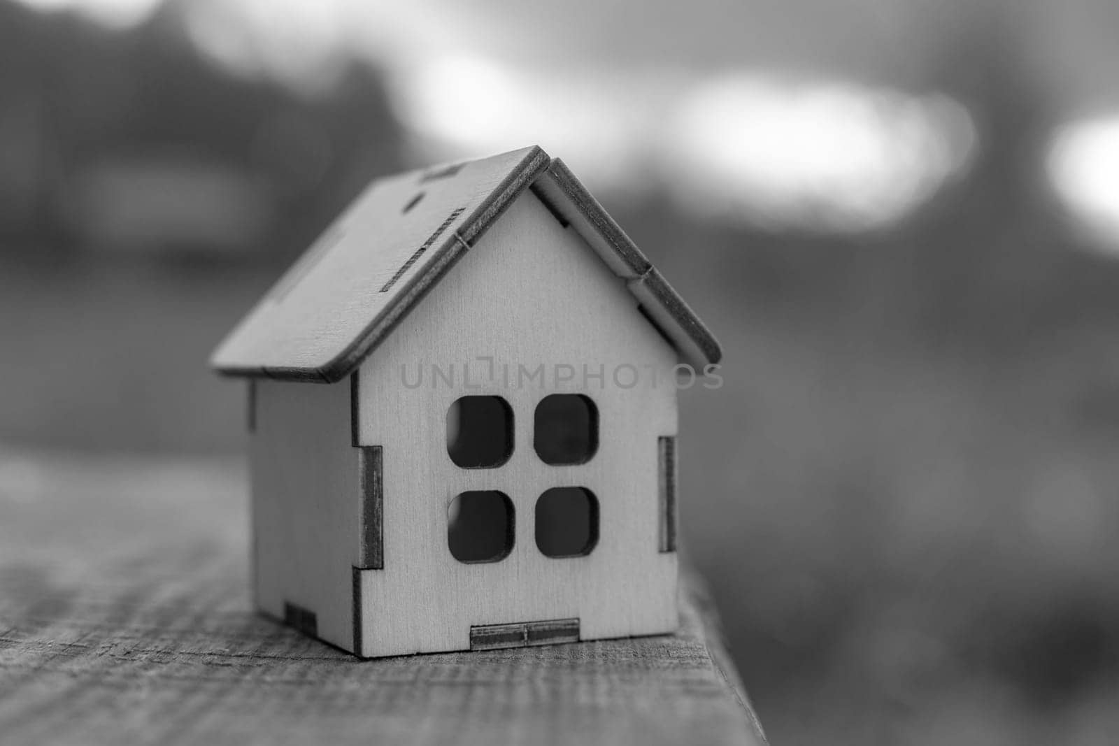 a small wooden toy house stands on the edge of a wooden table, may fall down. Monochrome. Copy space. Close up