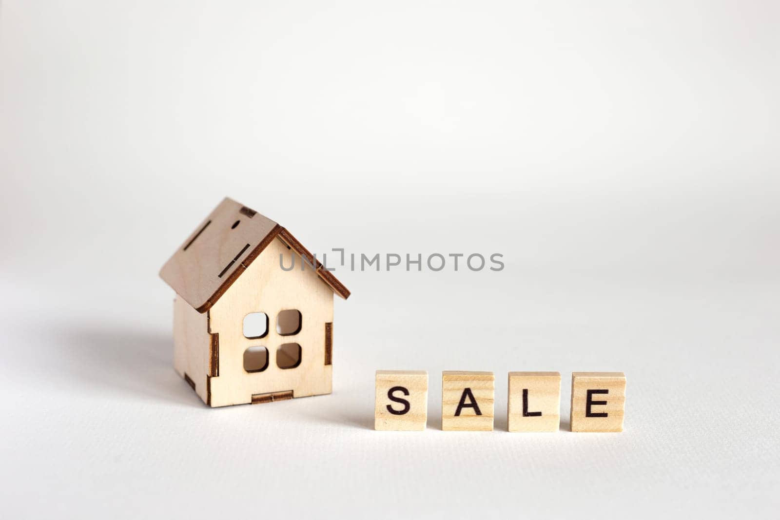 A small wooden toy house, stands on a white background and an inscription from wooden letters Sale. Copy space. Close up