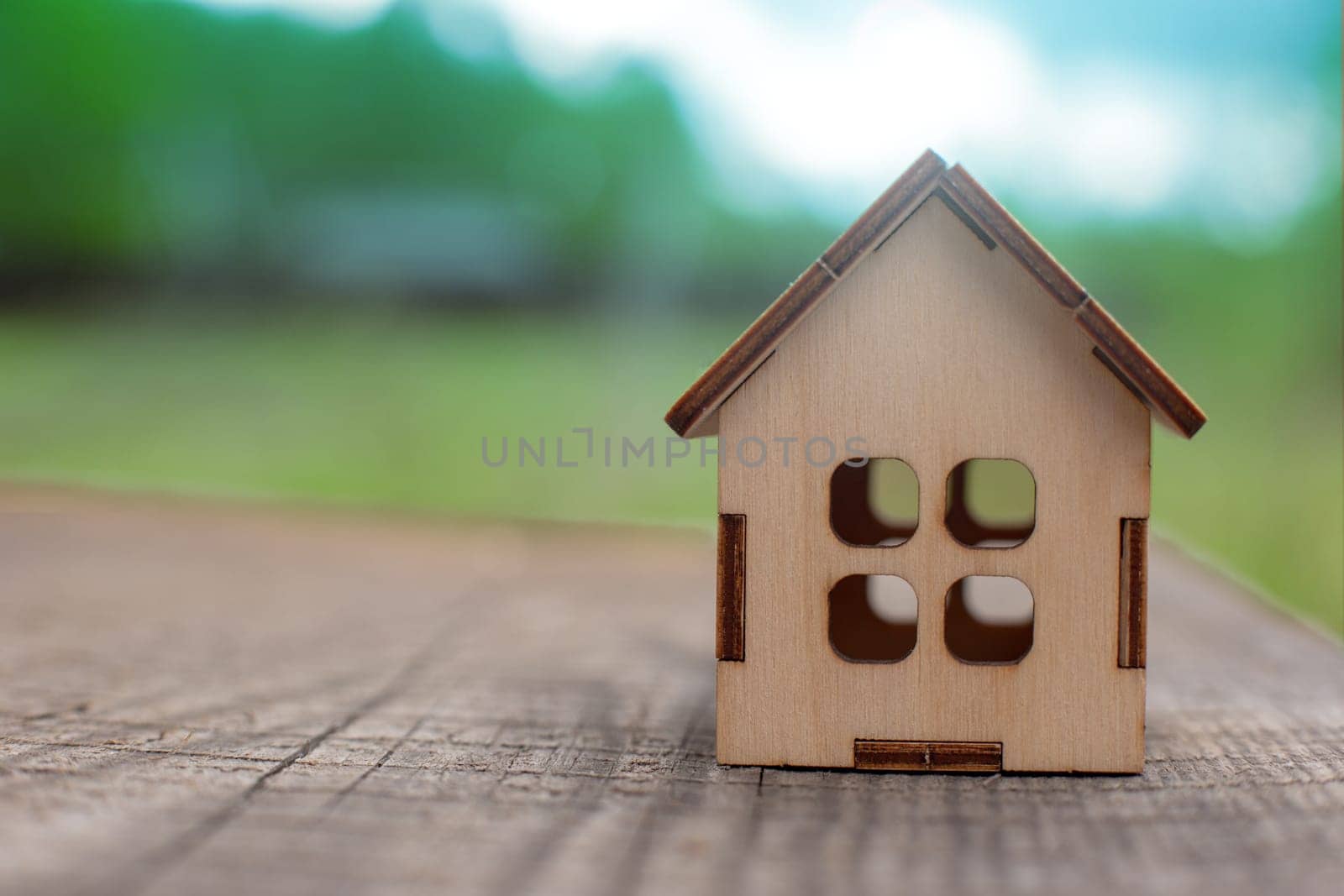 small wooden toy house stand on a wooden table on the background of green spring nature. Copy space. Close up