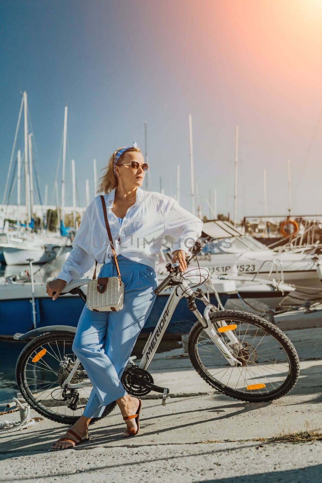 Woman enjoys bike ride along waterfront, Marina surroundings. She is wearing a white shirt and blue jeans, and she has a handbag with her. Capturing outdoor bike ride by waterfront. by Matiunina