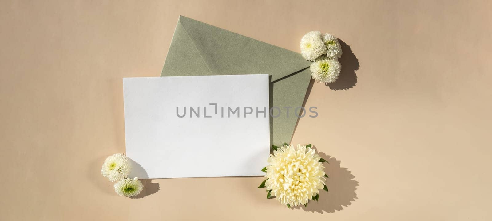 Beautiful little white flowers on postal green envelope on beige background, empty paper note copy space for text, spring time, greeting card for holiday. Flower delivery concept