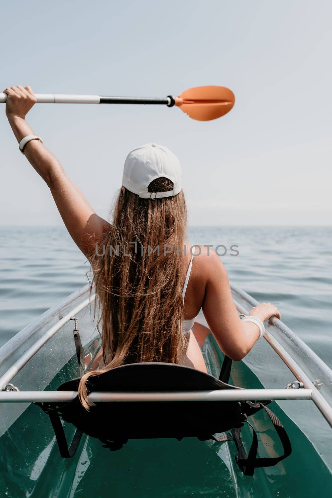 Woman in kayak back view. Happy young woman with long hair floating in transparent kayak on the crystal clear sea. Summer holiday vacation and cheerful female people having fun on the boat.