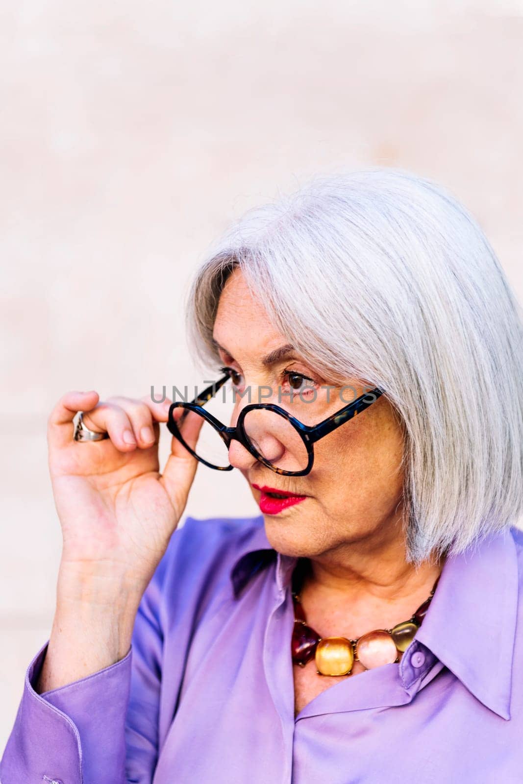portrait of a friendly surprised senior woman looking at camera over her glasses, concept of elderly people happiness and active lifestyle, copy space for text