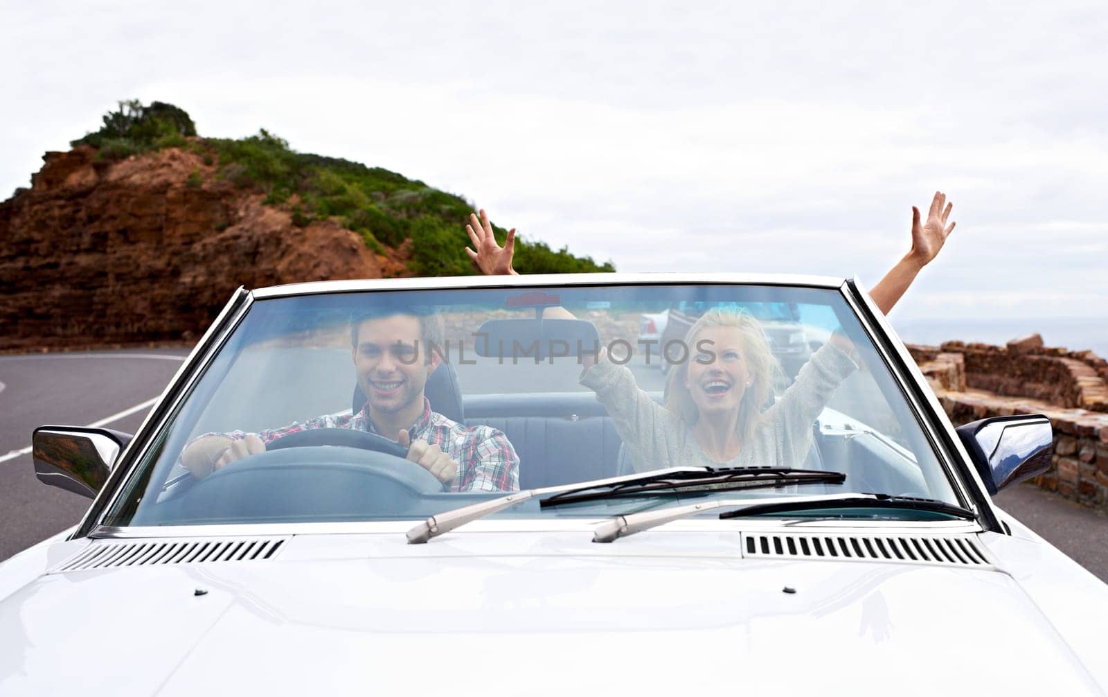 Couple, driving and convertible or excited or travel on mountain road or weekend trip, adventure or journey. Man, woman and transportation on hill in California or summer tourism, holiday or vacation by YuriArcurs
