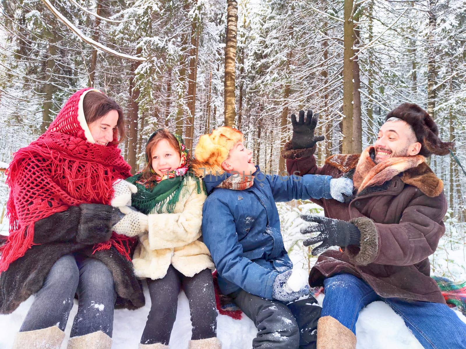 Joyful family ethnic dress with shawls and earflap hats in winter forest in carnival Maslenitsa in Russia. Tourists in Shrovetide in spring. Mother, father, son, daughter having fun in the snow