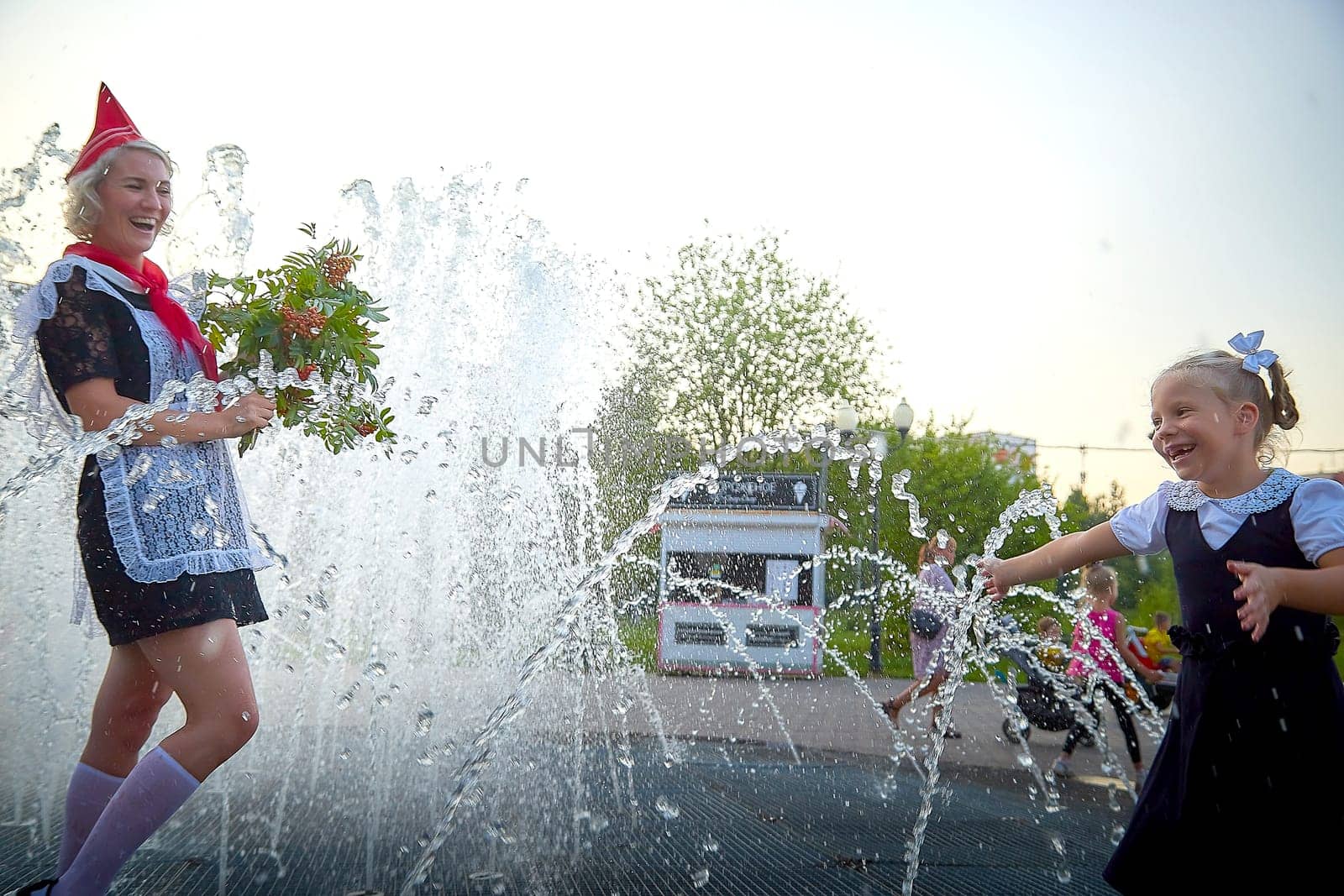 Young and adult schoolgirl on September with flowers having fun near water of fontain. Generations of schoolchildren, pioneer of USSR and October girl in modern uniform of Russia. Mom and daughter