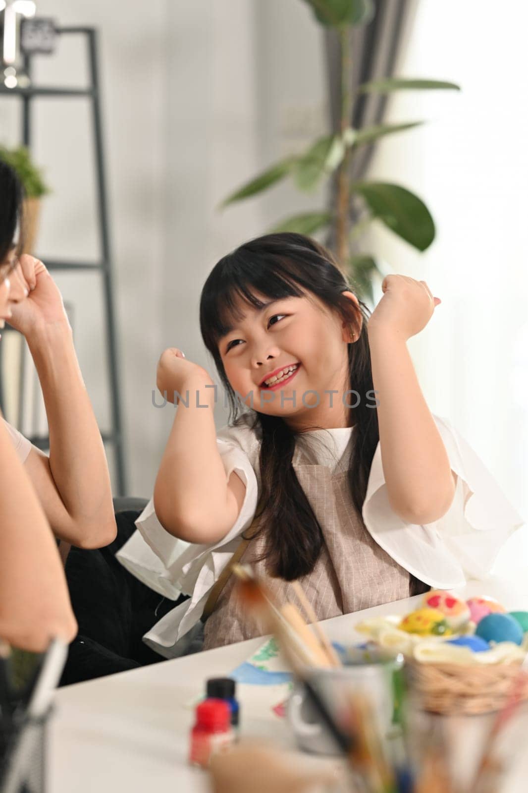 Cheerful little child girl painting eggs with mother, preparing for Easter holiday at home together by prathanchorruangsak