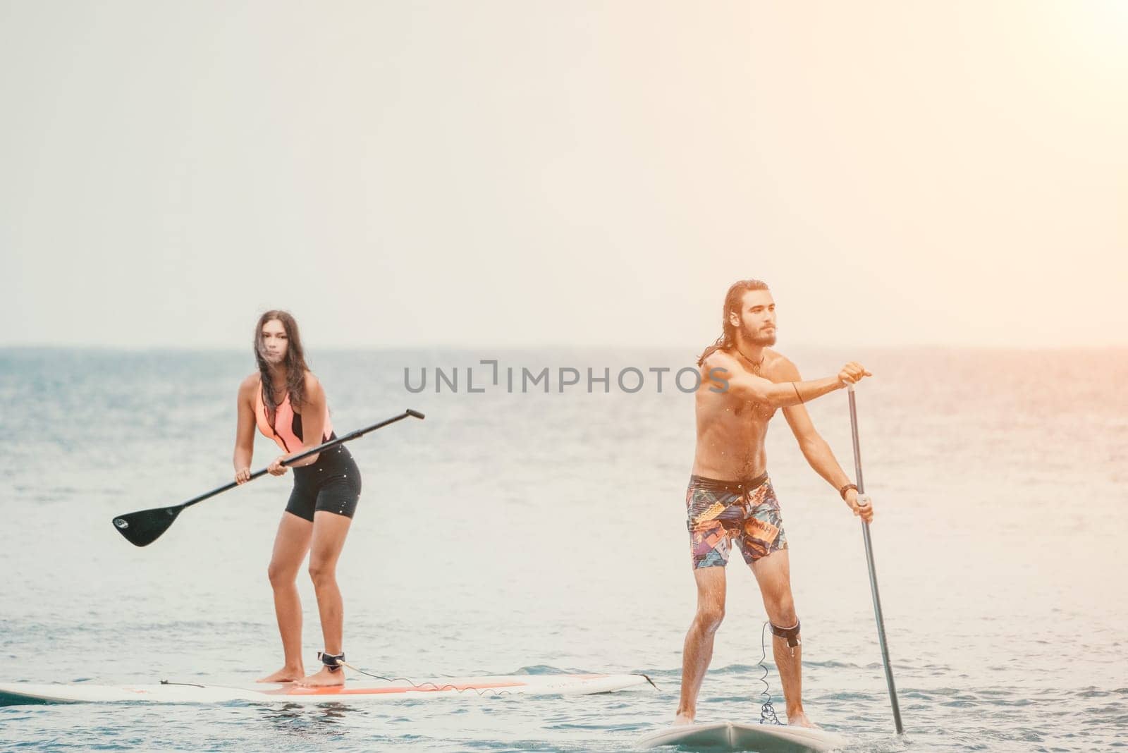 Sea woman and man on sup. Silhouette of happy young woman and man, surfing on SUP board, confident paddling through water surface. Idyllic sunset. Active lifestyle at sea or river