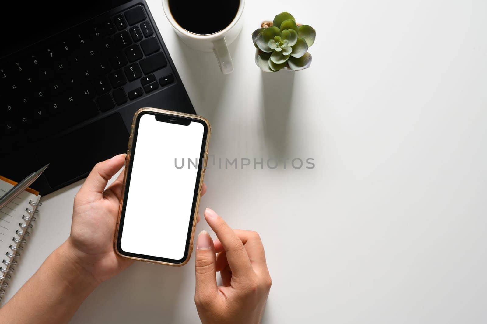 Woman using mobile phone at working desk. Top view, blank screen for your advertising text.