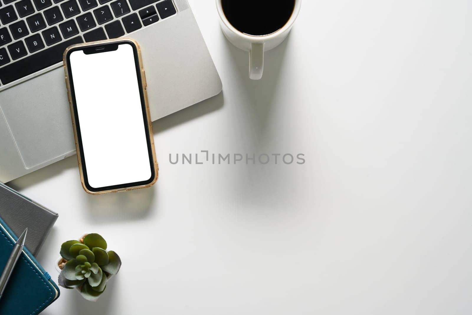Top view of smartphone with empty screen, laptop and a coffee cup on white table by prathanchorruangsak