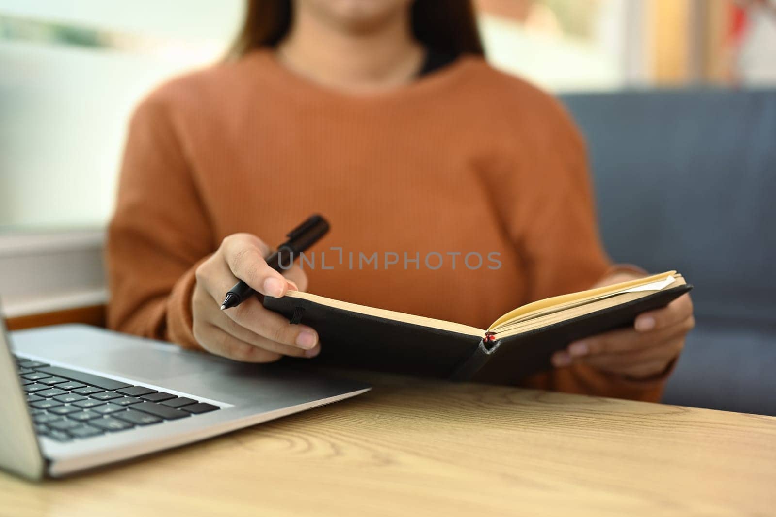 Young woman using laptop and reading notes or checking schedule.