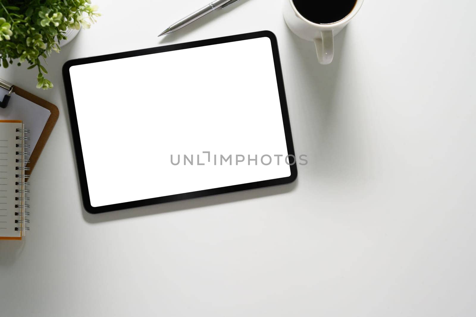 Digital tablet with empty screen, coffee cup and notepad on white table by prathanchorruangsak