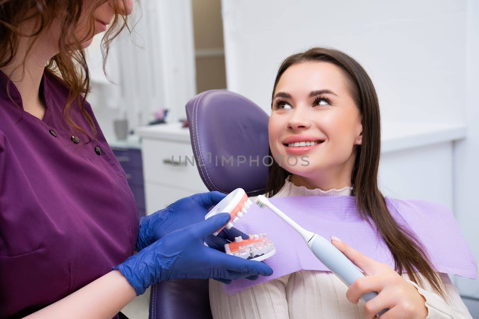 Dental professional explains to female patient how to brush teeth correctly in clinic. Dentists uses human jaw dental model for clarity