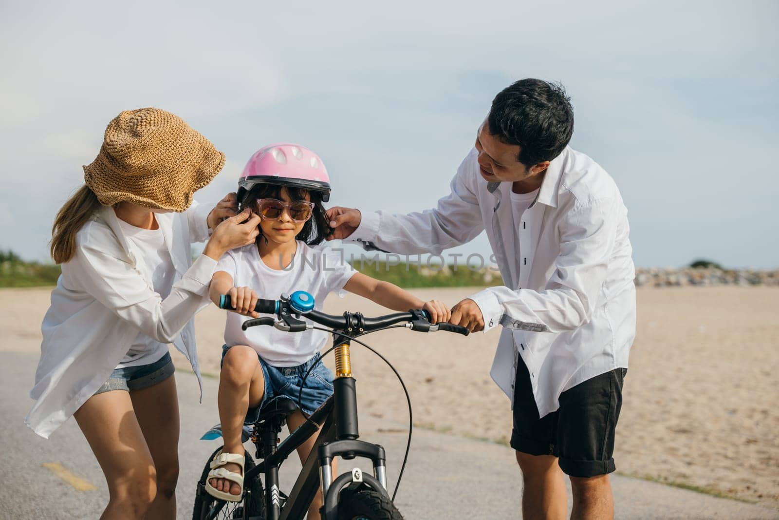 Under summer sun cheerful family enjoys road trip on sandy beach teaching and learning to ride bicycles. Safety laughter and spirit of childhood adventure define this heartwarming family scene. by Sorapop