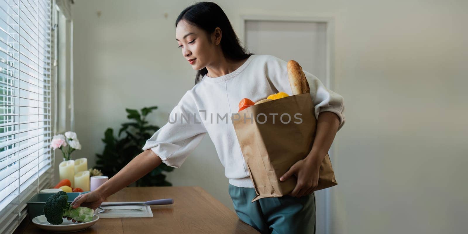Organic Food Delivery. Happy young woman unpacking bag with Fresh Vegetables in kitchen.