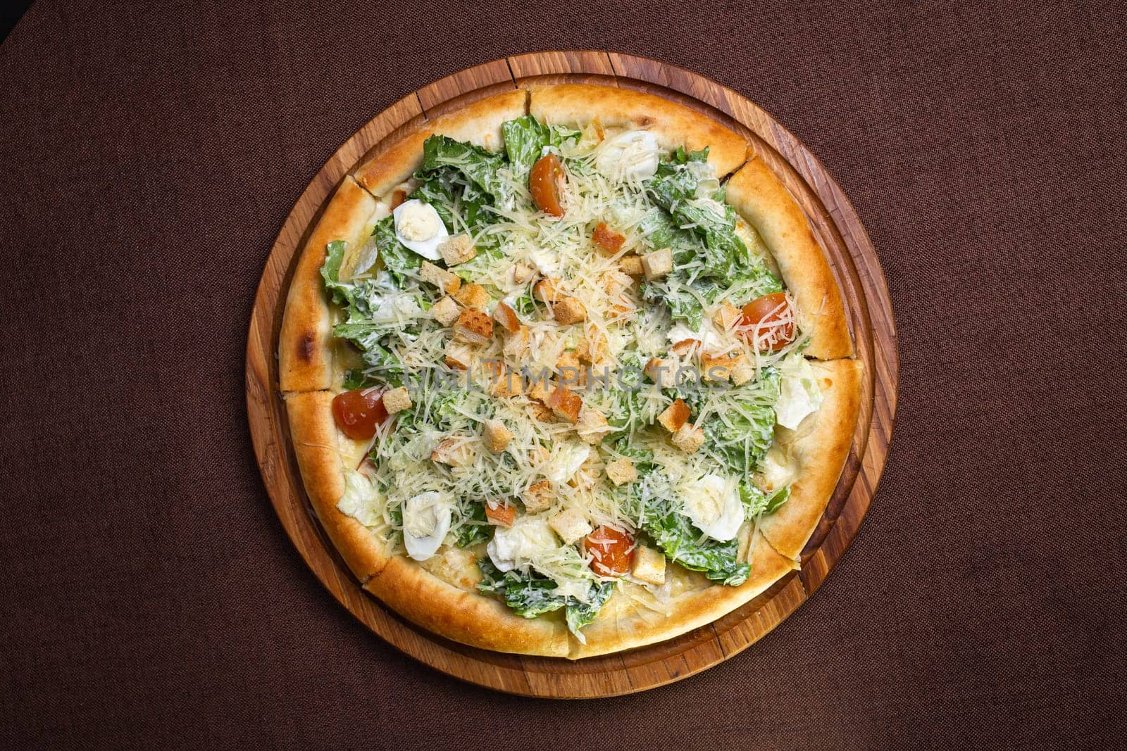 Round pizza with salad, tomatoes, cheese, croutons on wooden board. Brown background, top view. by Pukhovskiy