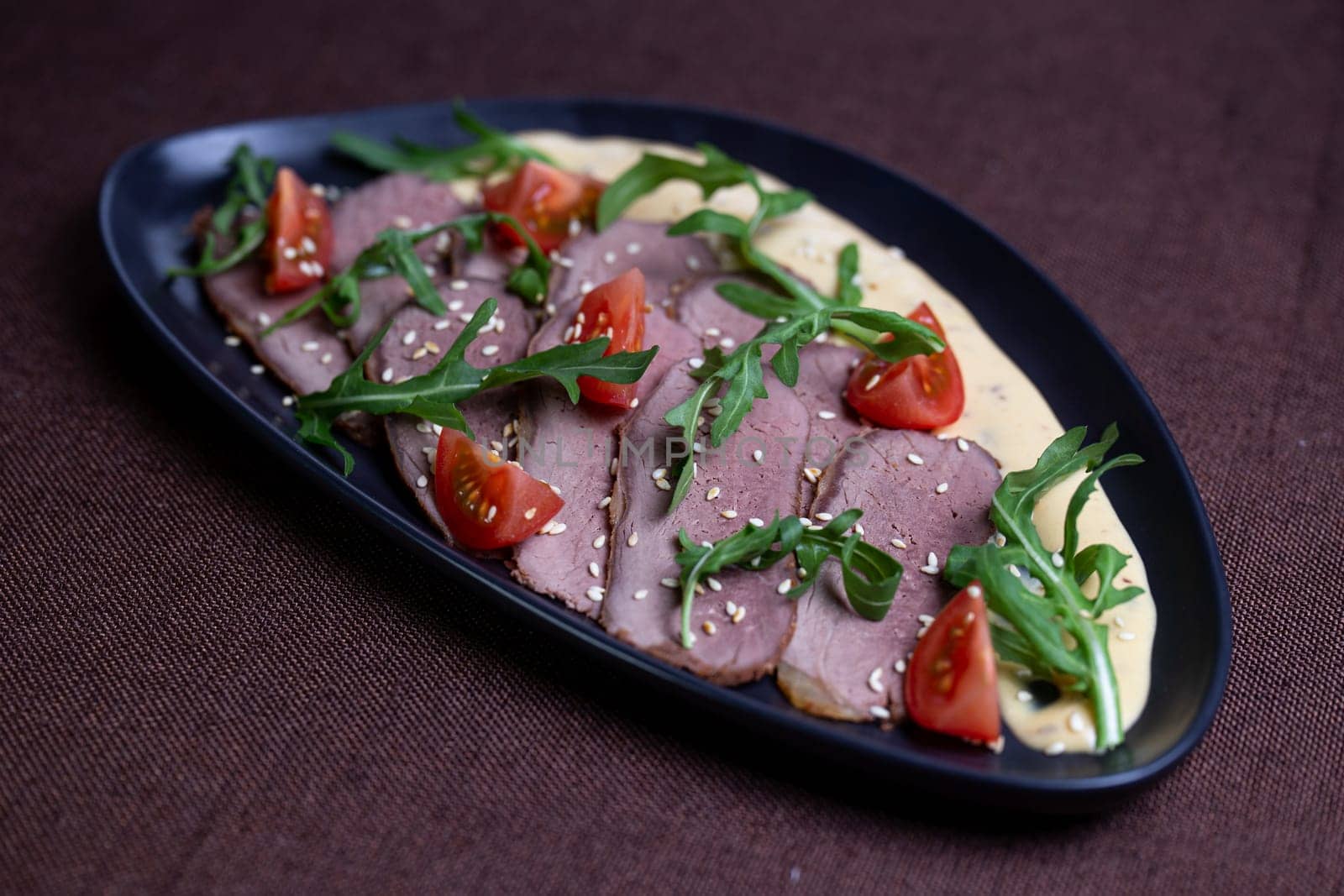 Savor the succulent flavors of pan-seared duck breast served with a vibrant arugula salad topped with cherry tomatoes, sprinkled with toasted sesame seeds, and drizzled with a luscious creamy sauce.