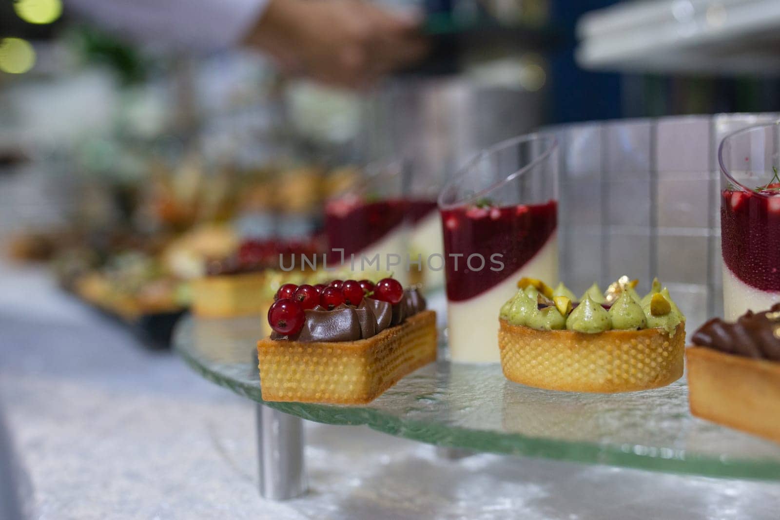 Variety of sweet and savory canapes and desserts displayed on glass shelf. Canapes topped with ingredients like caviar, salmon, and vegetables. Desserts include tarts, cakes, and pastries.