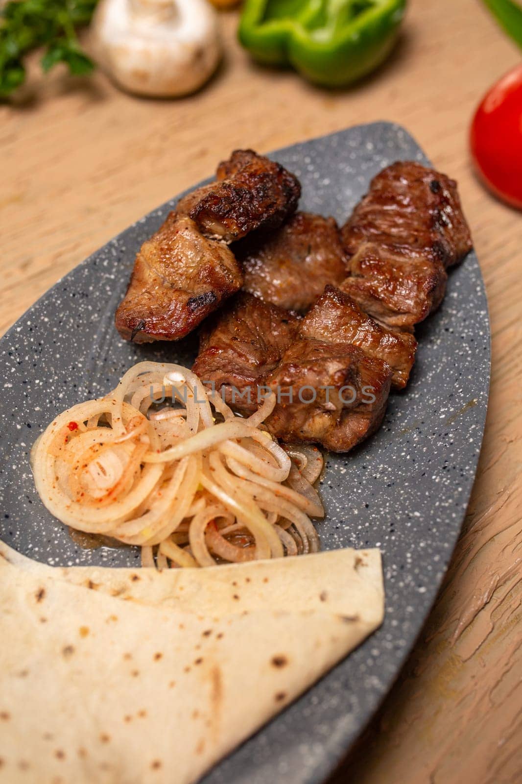 Grilled meat and vegetables on a rustic wooden table with soft flatbread. Succulent meat, tender veggies, vibrant tomatoes, peppers, mushrooms, onions create a delicious meal.