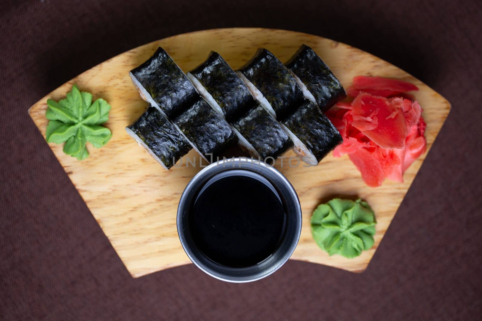 Sushi assortment featuring a variety of rolls and sashimi beautifully arranged on a wooden plate, accompanied by chopsticks and a side of savory soy sauce. Elegant presentation on a white background.