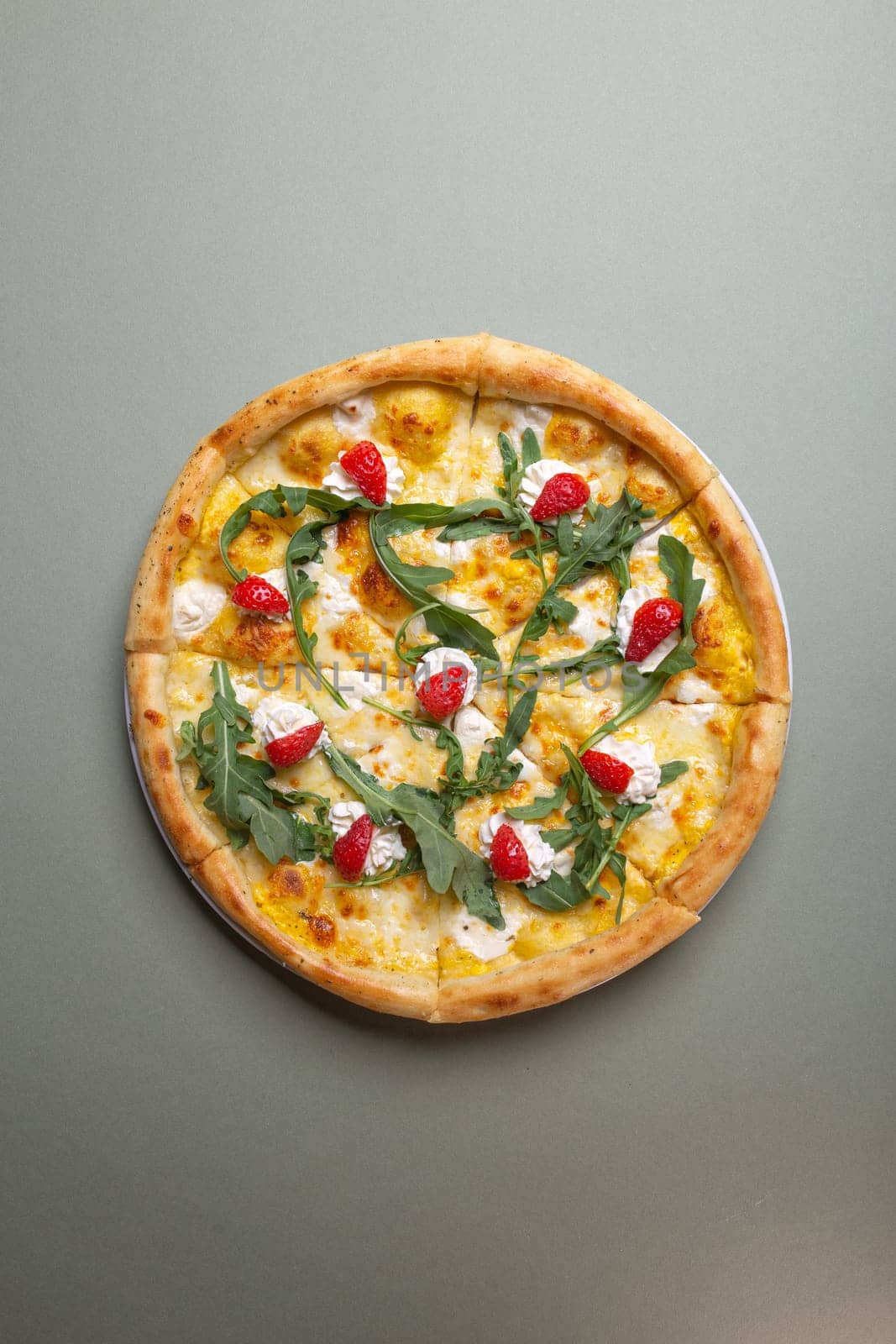 A delicious pizza with strawberries, cream cheese, and arugula on a white plate. The pizza is isolated on a green background. The pizza is perfect for a summer party or a picnic.