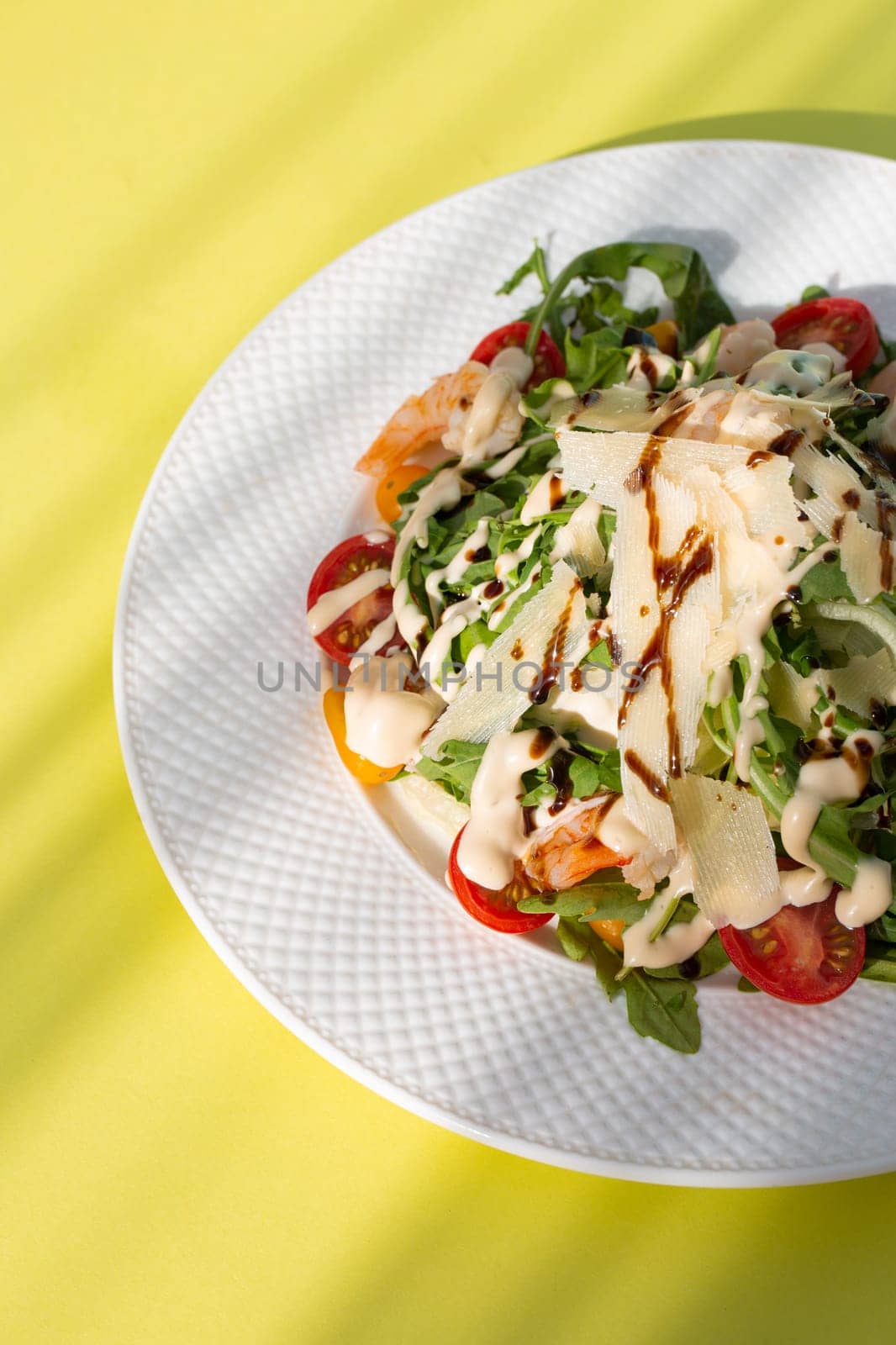 Fresh salad with greens, tomatoes, grilled shrimps on white plate. Top view on yellow background. by Pukhovskiy