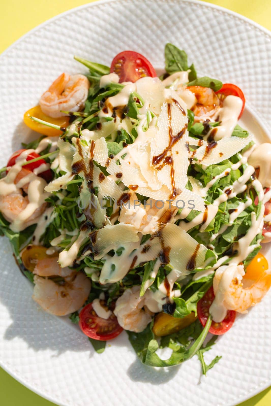 Fresh salad with greens, tomatoes, grilled shrimps on white plate. Top view on yellow background. by Pukhovskiy