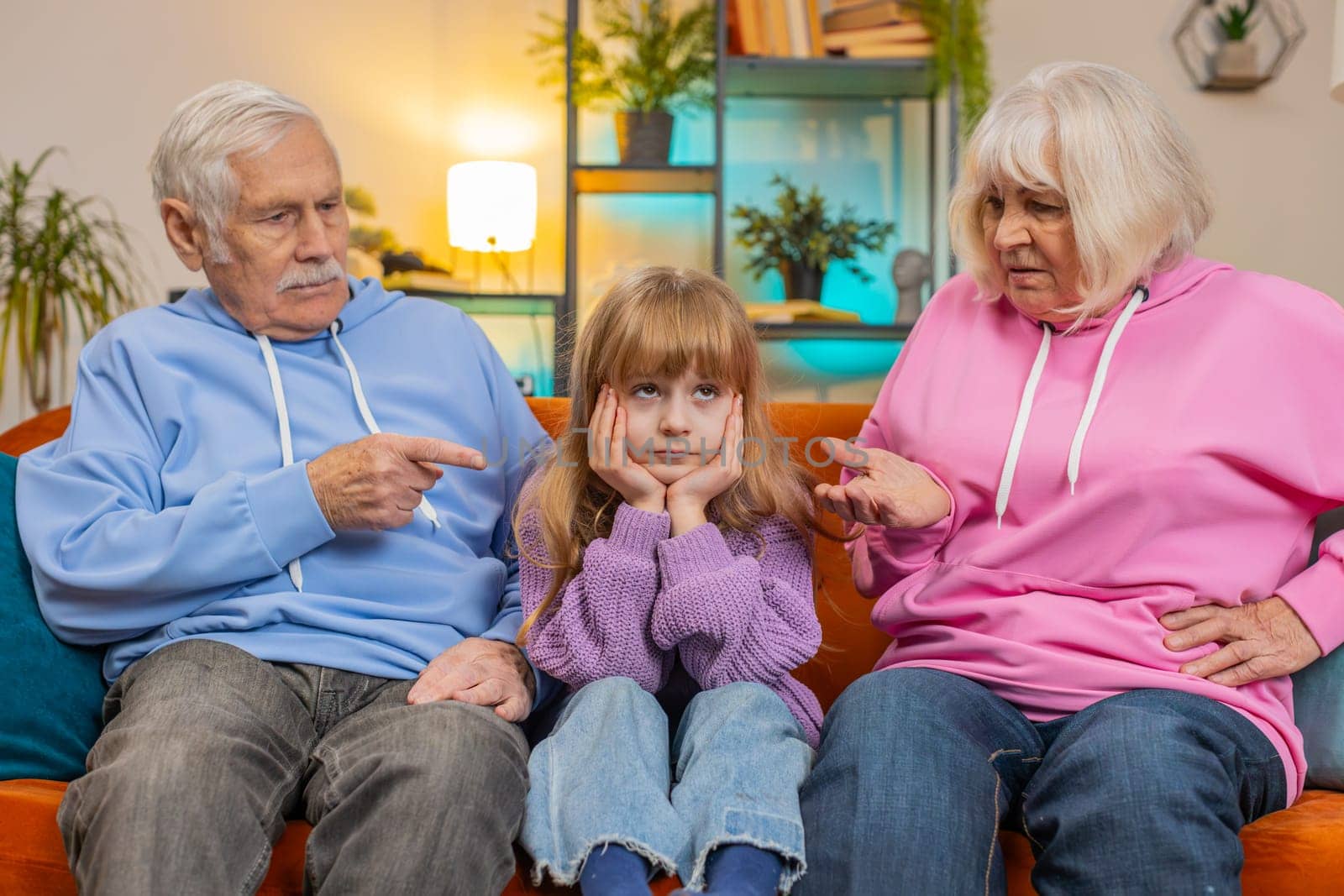 Irritated grandfather and grandmother scolding granddaughter for bad behavior and disobedience on sofa, raising voice scream at little grandchild. Difficulties of upbringing, misbehaved child concept