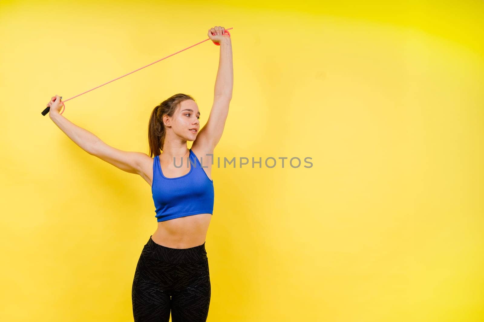 Portrait of gentle muscular woman holding skipping rope on her neck over yellow background