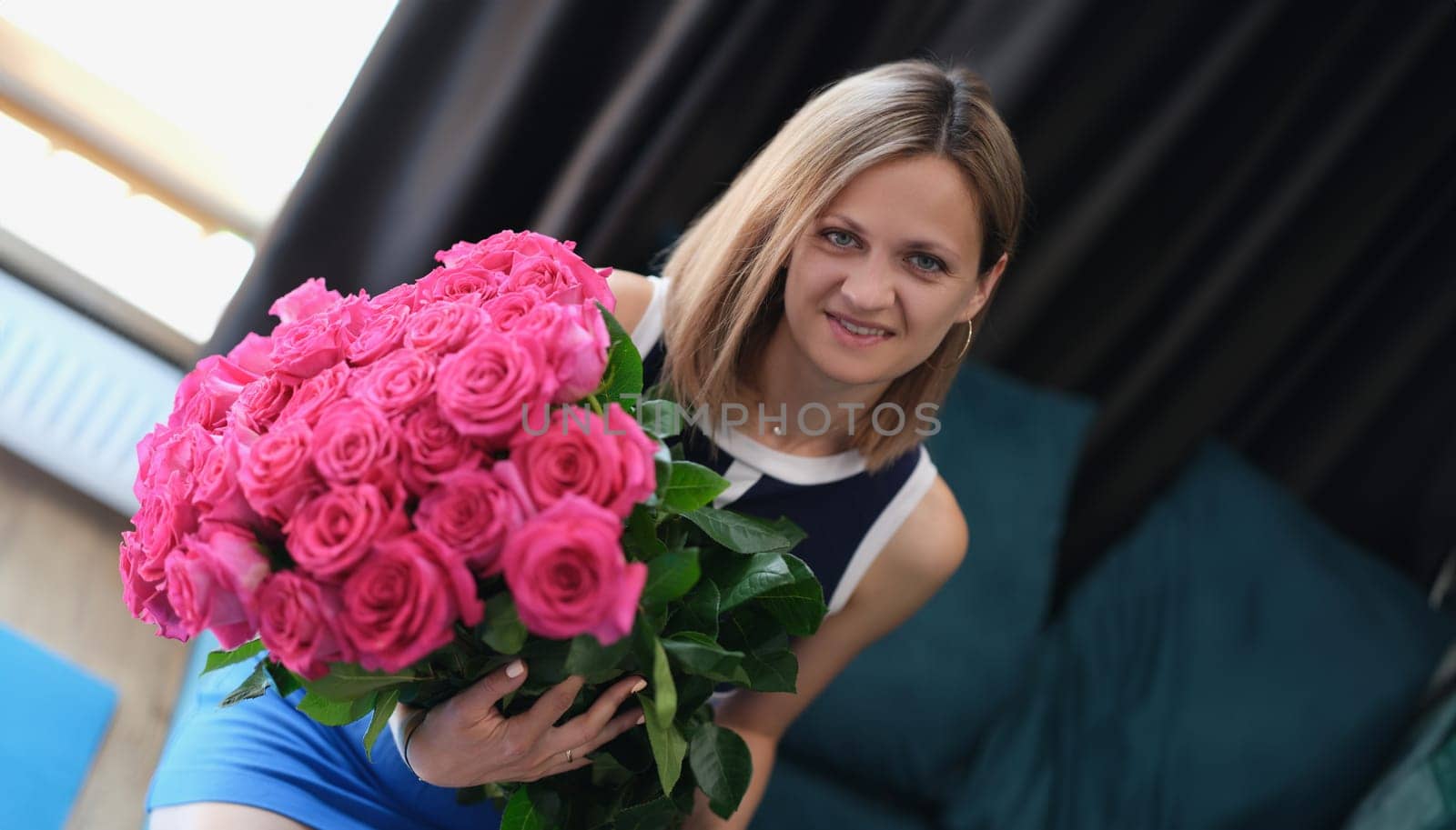 Young woman sitting on sofa and holding large bouquet of roses. Flower delivery concept