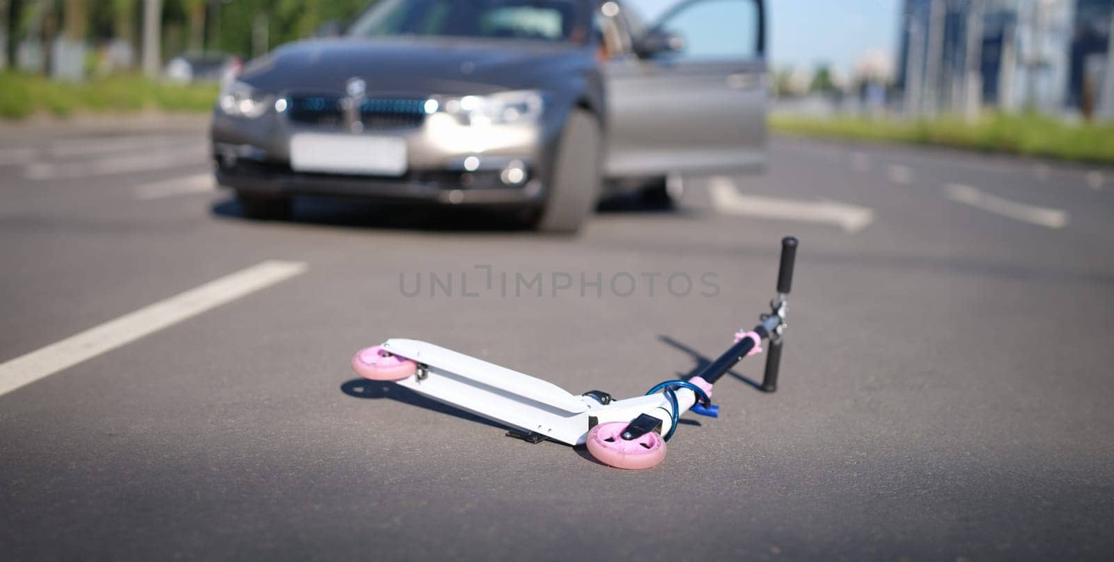 Children scooter lying on road near car closeup. Traffic accidents with children concept