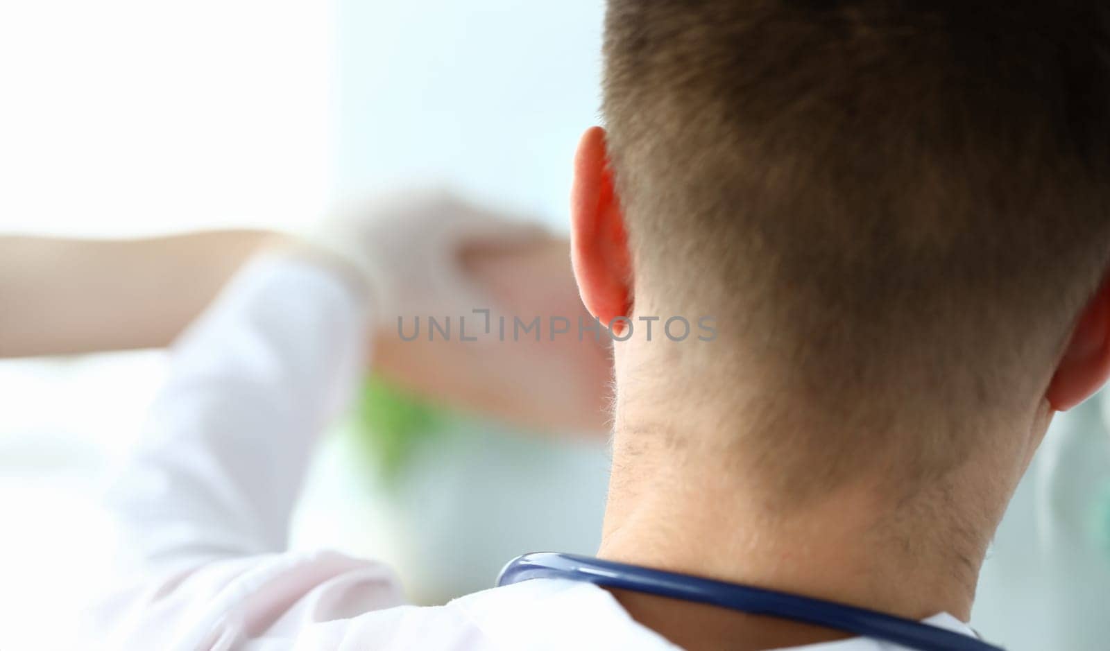 Rear view doctor in gloves examining patients skin. Allergy to medicine or fungal infections. Affordable modern health care. Doctor stands in white coat with stethoscope on her neck
