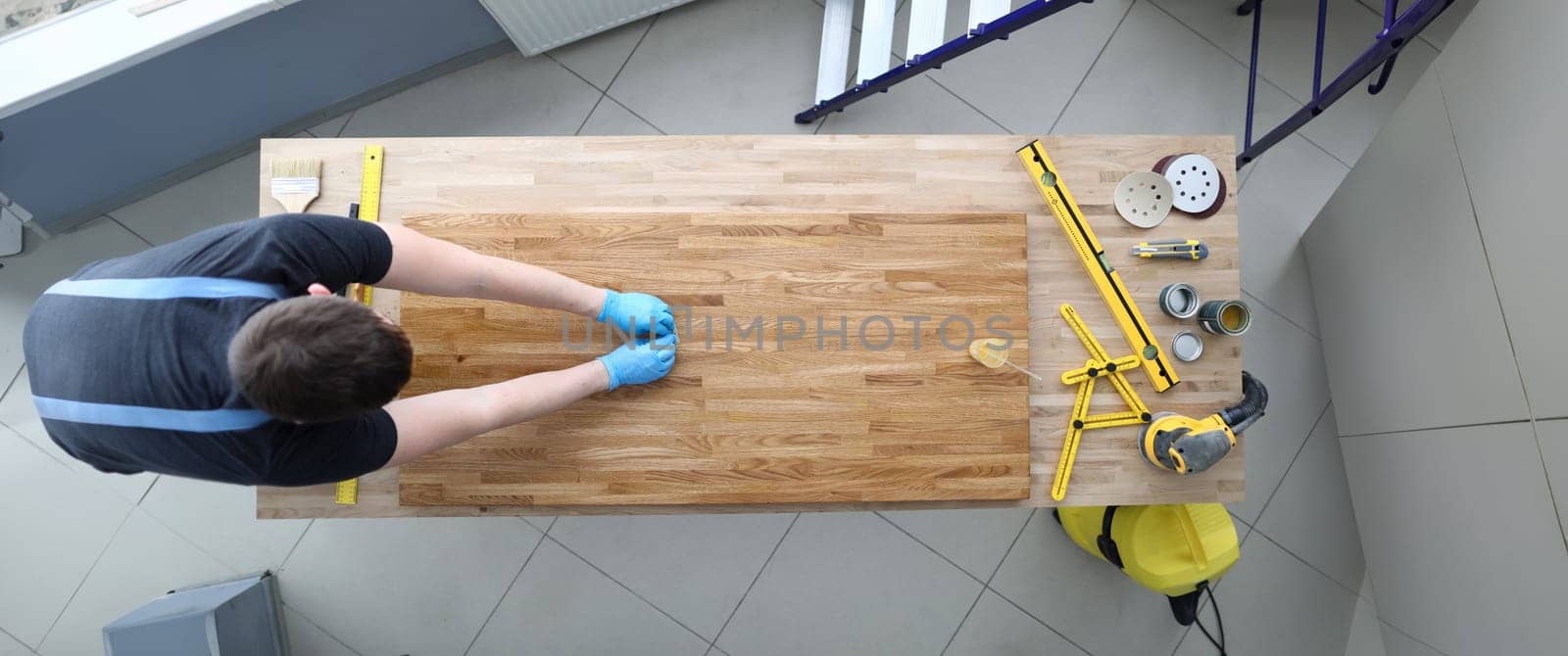 Top view of construction worker polishing wood. Male in protective gloves. Tools and sander machine on other side of table. Renovation and carpenter job concept