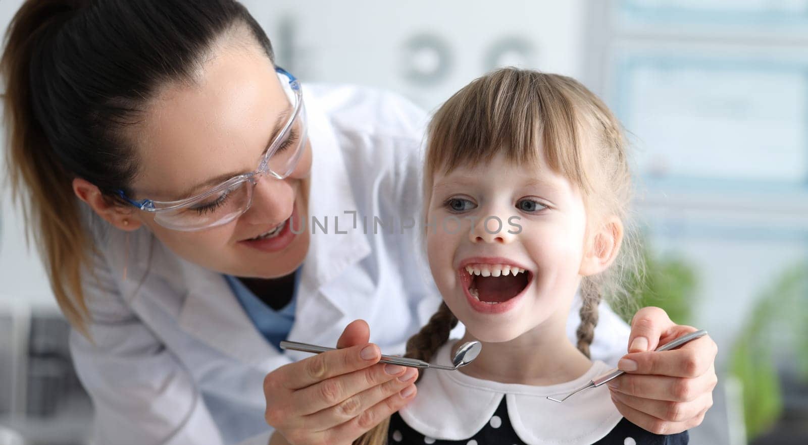 Woman dentist examines teeth in clinic at child by kuprevich