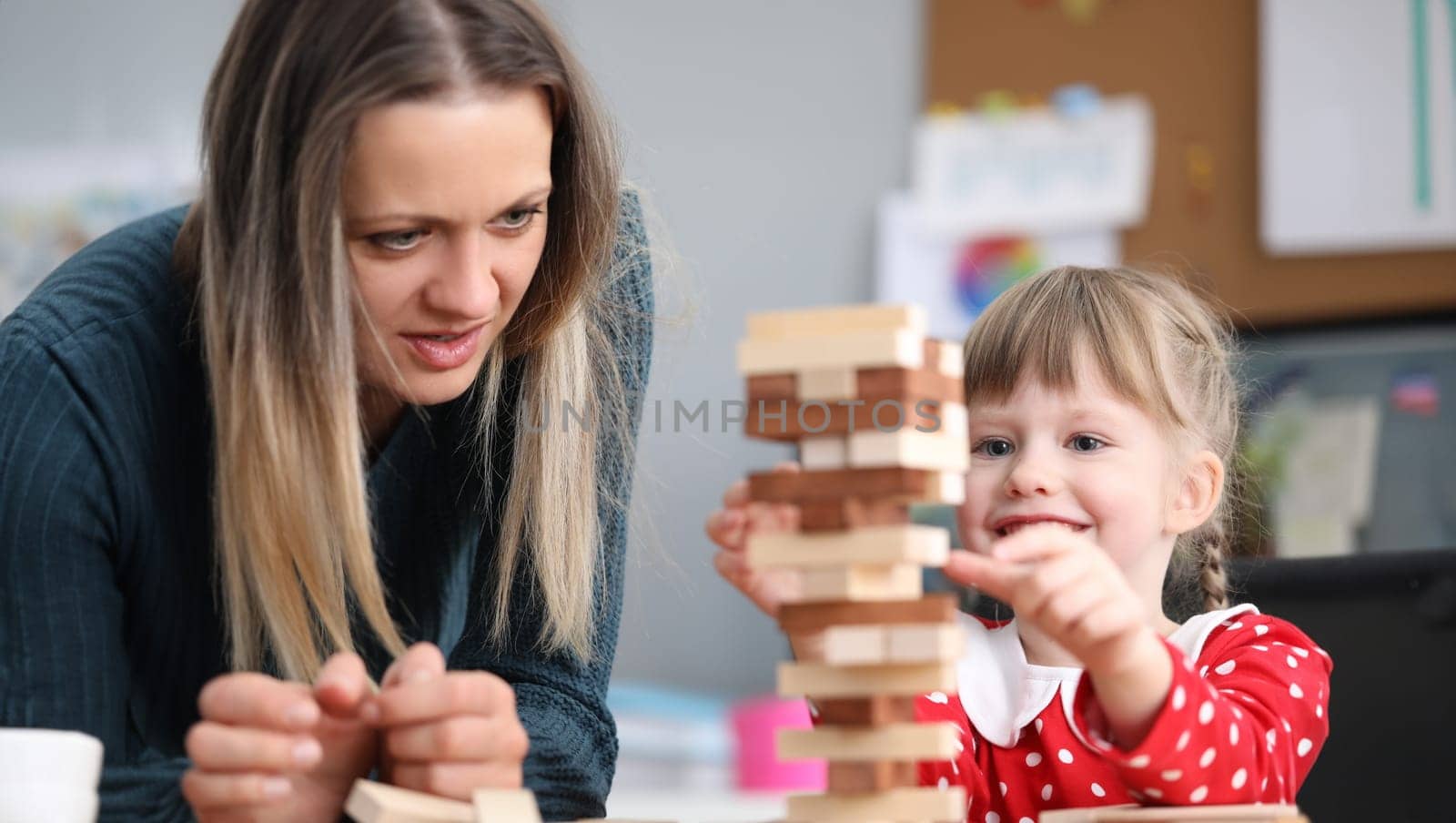 Mom and daughter stack blocks on top each other. Child is taught to choose right subject. Girl movements are awkward, inept and inharmonious. Children and adults communicate, play