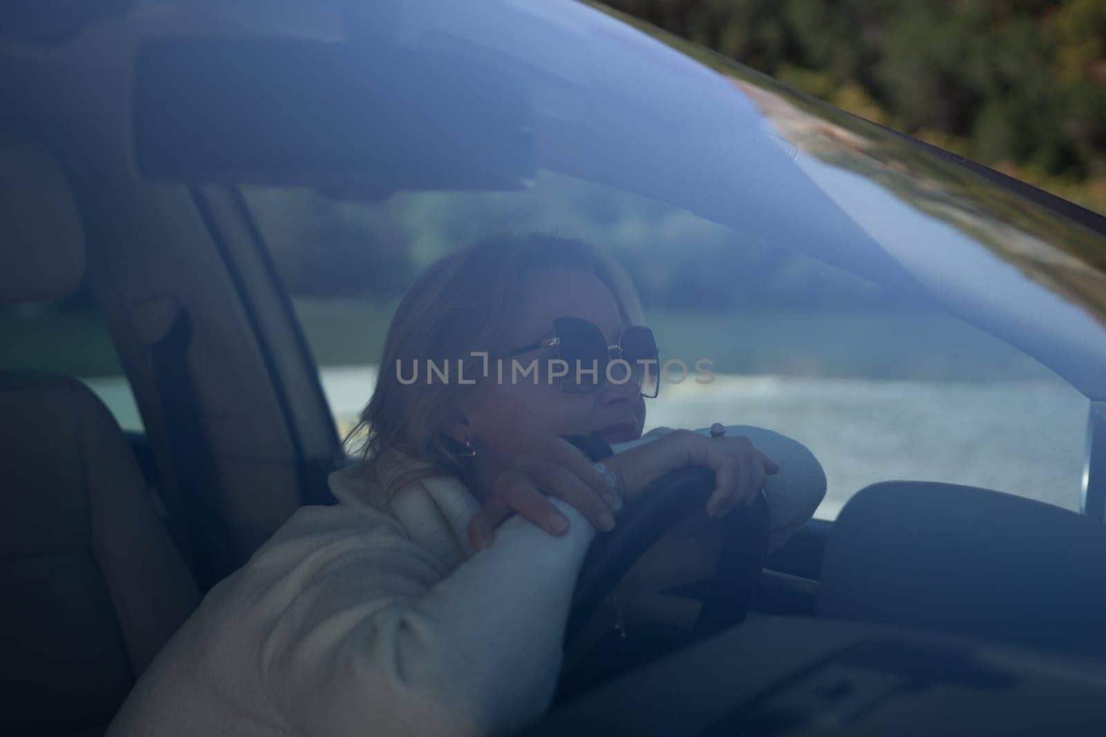 A blonde woman in a white sweater and jeans is driving. Happy woman sitting in a car with a white interior