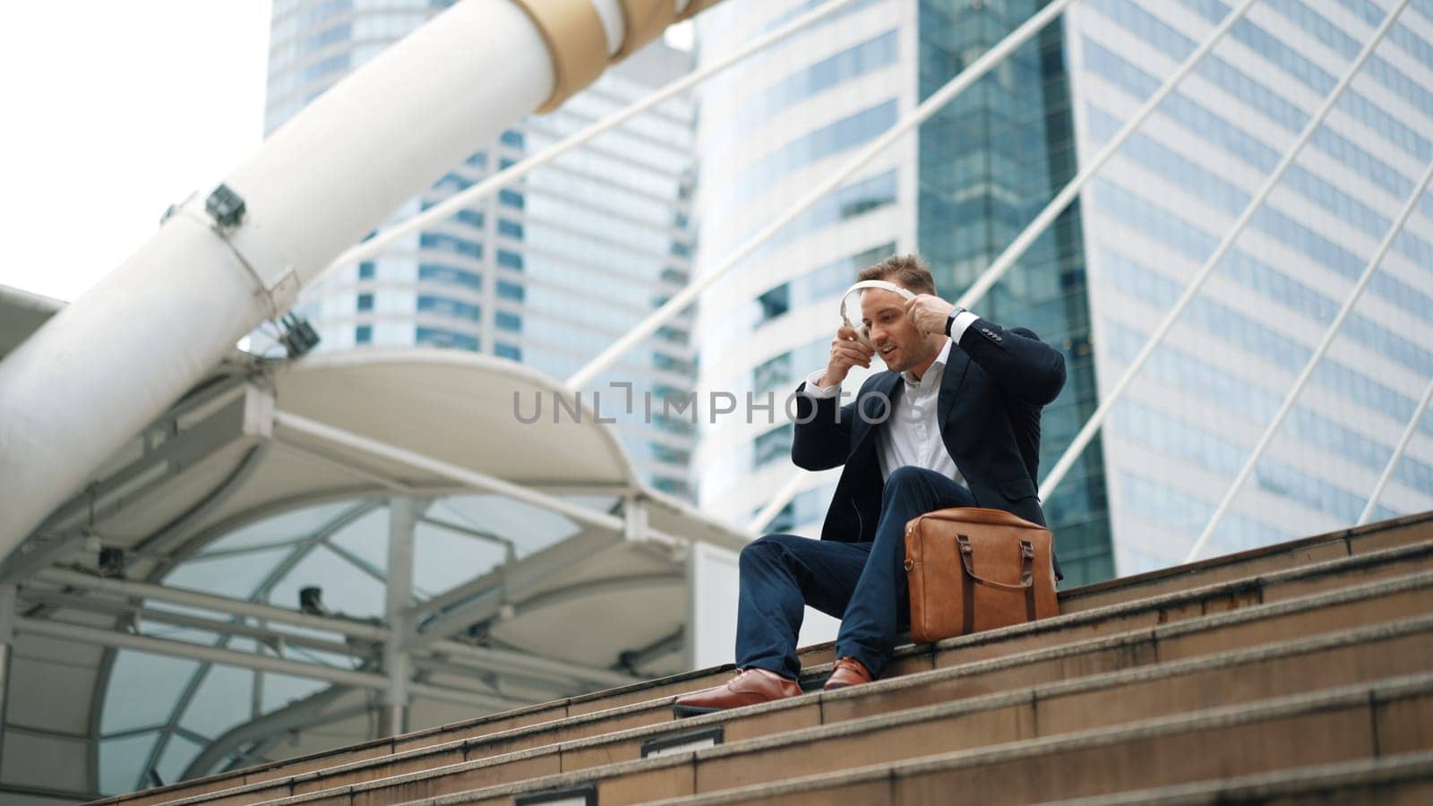 Smart business man wear headphone while sitting at stair in urban city. Urbane. by biancoblue